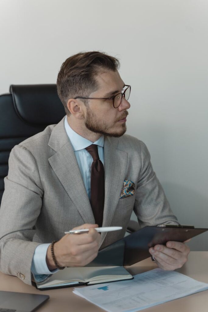 Businessman in a suit with clipboard and pen in an office environment.