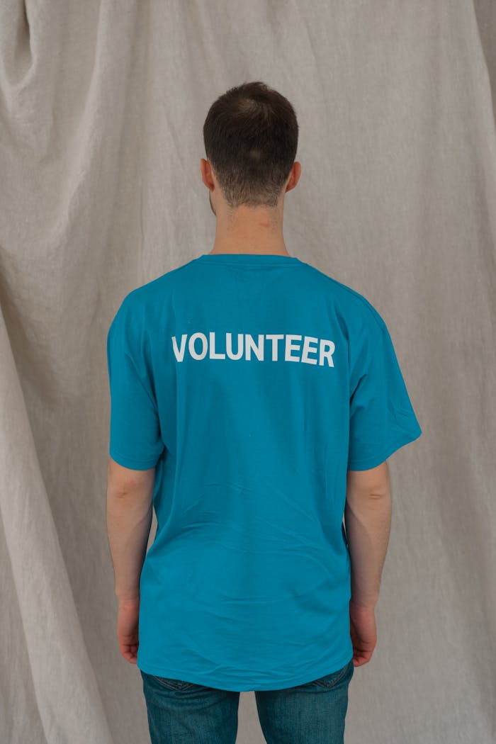 Person wearing a blue volunteer shirt standing against a neutral backdrop.